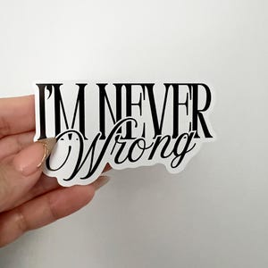 May include: A white sticker with the text "I'M NEVER Wrong" in black. The words "I'M NEVER" are in a bold, sans-serif font, while "Wrong" is in a cursive script. The sticker is rectangular.