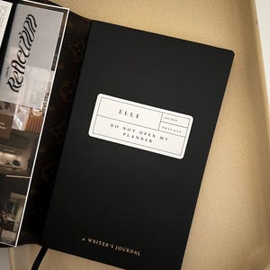 May include: Black leather-bound journal with the text "ELLE EST. 2010 PRIVATE DO NOT OPEN MY PLANNER" and "# WRITER'S JOURNAL" on the front cover.