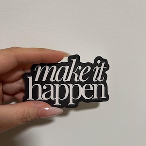 以下が含まれることがあります： 白のスタイリッシュなスクリプトで「make it happen」という言葉が書かれた黒いステッカー。ステッカーは丸みを帯びた長方形の形をしており、白い背景に対して保持されています。