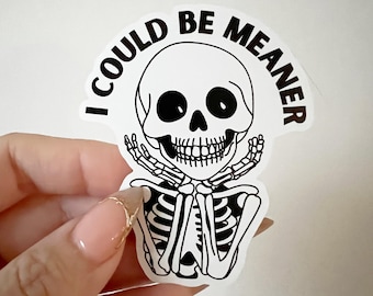May include: A white sticker featuring a black and white skeleton graphic. The skeleton is holding its hands up to its face. The text "I COULD BE MEANER" is arched above the skull.