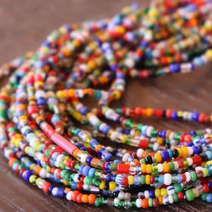 May include: A colorful beaded necklace made of small glass beads in various colors, including red, blue, green, yellow, and white. The beads are strung together on a thin cord and the necklace is long and flowing.