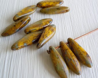 May include: A group of 9 yellow and brown glass beads with a mottled, marbled effect. The beads are oval shaped and have a glossy finish. The beads are strung on a copper wire.