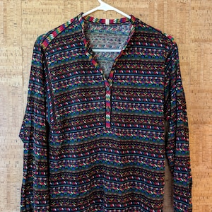 May include: A long-sleeved shirt with a black background and colorful geometric patterns. The shirt has a button-up collar and a relaxed fit.