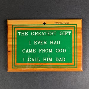 May include: Wooden sign with the text "THE GREATEST GIFT I EVER HAD CAME FROM GOD I CALL HIM DAD" in green lettering. The sign has a green border and the words "FORBIDDEN CAVERNS GREAT SMOKY MTNS" at the top. The sign is rectangular with a hole at the top.