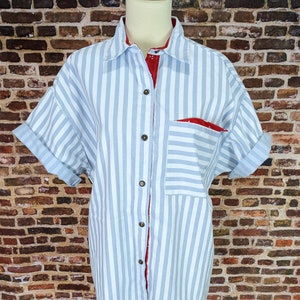 May include: A blue and white striped button-down shirt with a red and white striped lining. The shirt has a single pocket on the left side.