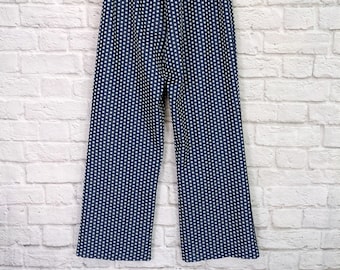 Puede incluir: Un pantalón de pierna ancha con un patrón de lunares blancos sobre un fondo azul marino. El pantalón tiene una cintura elástica y está colgado de una percha de madera.