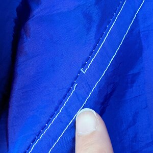 Puede incluir: Primer plano de una tela azul vibrante con una costura blanca. La tela tiene un ligero brillo y la costura corre diagonalmente por la imagen. La textura de la tela es visible.
