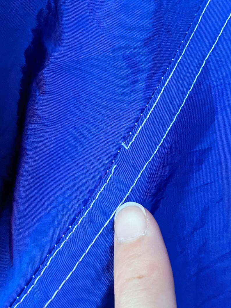 Puede incluir: Primer plano de una tela azul vibrante con una costura blanca. La tela tiene un ligero brillo y la costura corre diagonalmente por la imagen. La textura de la tela es visible.