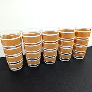 Puede incluir: Cinco vasos de tubo vintage. Cada vaso presenta un diseño de bandas marrones con rayas blancas. Los vasos son transparentes y tienen un diseño sencillo y elegante, ideal para servir bebidas.
