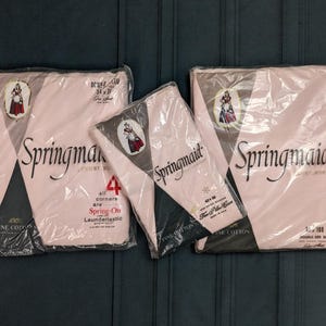 May include: Three packages of vintage Springmaid bed linens. The packages are wrapped in clear plastic and feature a pink and black design with the brand name in elegant script. The packages have the text "100% Fine Cotton".
