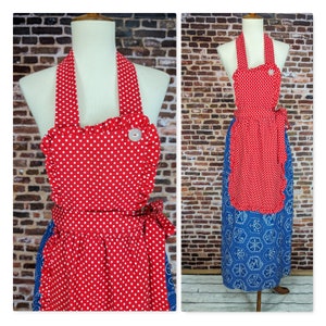 May include: A red and white polka dot apron with a ruffled top and a blue patterned bottom. The apron has a halter neck and a large white button detail. The apron is tied at the waist with a matching fabric tie.