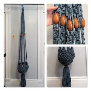 Puede incluir: Un macetero de macramé azul con cuentas de madera. El macetero está hecho de cordón de algodón y tiene un borla en la parte inferior. El macetero está colgado de un gancho en una pared blanca.