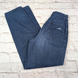 Puede incluir: Pantalones vaqueros de mezclilla azul oscuro con un sutil patrón de rayas verticales. Los pantalones tienen un diseño de cintura alta, un bolsillo trasero con el texto bordado Chic en hilo azul claro, cierre de botón y cremallera.