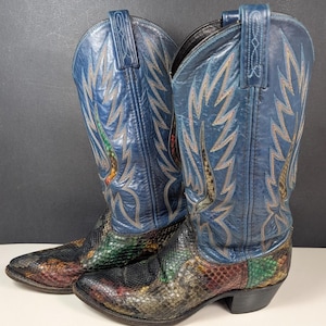 Puede incluir: Un par de botas vaqueras con cañas de cuero azul con costuras decorativas y empeines con textura de piel de serpiente multicolor. Las botas tienen punteras puntiagudas, tacones apilados y tiradores en la parte superior, con una mezcla de escamas verdes, rojas y negras.