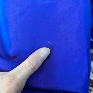 Puede incluir: Primer plano de una tela azul vibrante, posiblemente nailon o un material similar. La textura parece suave con l&iacute;neas sutiles. Una mano es parcialmente visible, tocando la tela. La impresi&oacute;n general es de un color s&oacute;lido y saturado.