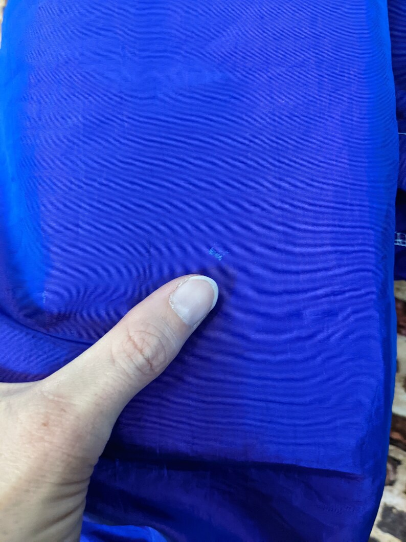 Puede incluir: Primer plano de una tela azul vibrante, posiblemente nailon o un material similar. La textura parece suave con l&iacute;neas sutiles. Una mano es parcialmente visible, tocando la tela. La impresi&oacute;n general es de un color s&oacute;lido y saturado.