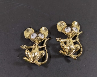 May include: Two gold-tone mouse brooches with large white eyes. The mice are sitting up with their tails curled behind them.