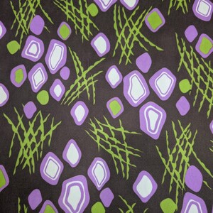 May include: A fabric with a repeating pattern of purple, white, and green shapes on a dark brown background. The design includes diamond shapes with white centers, green circles, and green, crisscrossing lines.