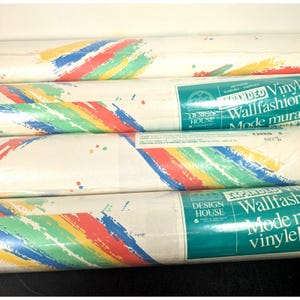 May include: Several rolls of wallpaper with a white background and colorful brushstroke designs in red, yellow, green, and blue. The rolls are labeled "Expanded Vinyl Wallfashion Mode murale" and "Design House". Each roll is 64.5 inches long.