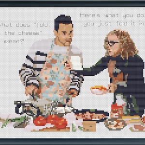 May include: Cross-stitch artwork depicting two people in a kitchen setting. One person, wearing an apron, asks "What does 'fold in the cheese' mean?" The other replies, "Here's what you do... you just fold it in." The image is framed.