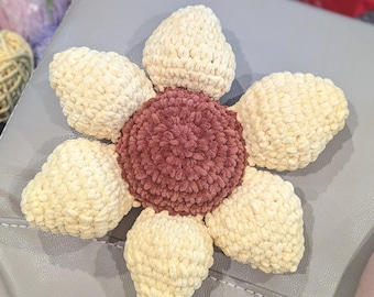 May include: A crocheted flower with a brown center and cream-colored petals. The flower is made with a soft, fuzzy yarn.