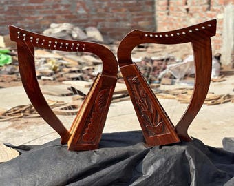 Puede incluir: Dos arpas de madera tallada, de color marrón oscuro. Cada una presenta intrincados grabados florales en la caja de resonancia y pequeñas clavijas decorativas en el mástil curvo. Fondo borroso.