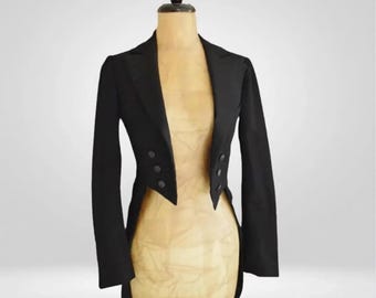 May include: A black tailcoat jacket displayed on a mannequin. The jacket features a notched lapel, long sleeves, and three buttons on each side. The back of the jacket has a split tail design. The mannequin is a light tan color, and the background is plain.