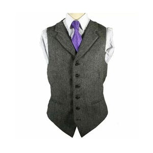 May include: A gray tweed vest with a notched lapel and a five-button closure. A white dress shirt and a purple tie are visible underneath the vest. The vest has two front pockets and a tailored fit.