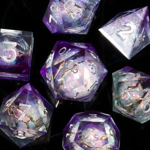 May include: Set of seven polyhedral dice with a purple and clear resin design. The dice have silver numbering and a shimmering, iridescent interior. The dice are designed for tabletop role-playing games.