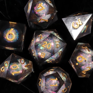 May include: A set of seven polyhedral dice made of clear resin with iridescent, multi-coloured glitter suspended inside. Each die features gold-coloured engraved numbers. The set includes a d20, d12, d10, d8, d6, d4, and a percentile die.