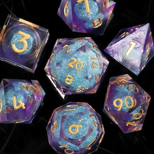 May include: A set of seven polyhedral dice with a clear, iridescent purple and blue design. Each die has gold-coloured numbers. The dice are arranged in a circular pattern, ideal for tabletop gaming.