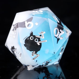 May include: A twenty-sided die with a blue and white gradient. The die features black cat silhouettes and silver-colored numbers. The die is made of a clear, translucent material, and is designed for tabletop gaming.