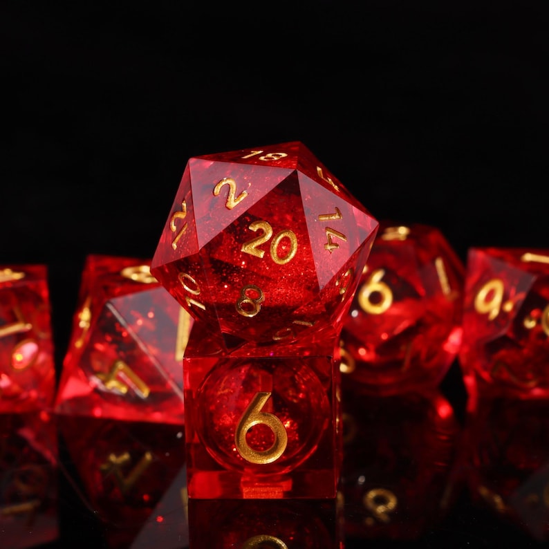 May include: A set of red, multi-sided dice with gold numbering. The dice are transparent, with a glittery effect. The image is a close-up, showing the detail of the dice, including a twenty-sided die.