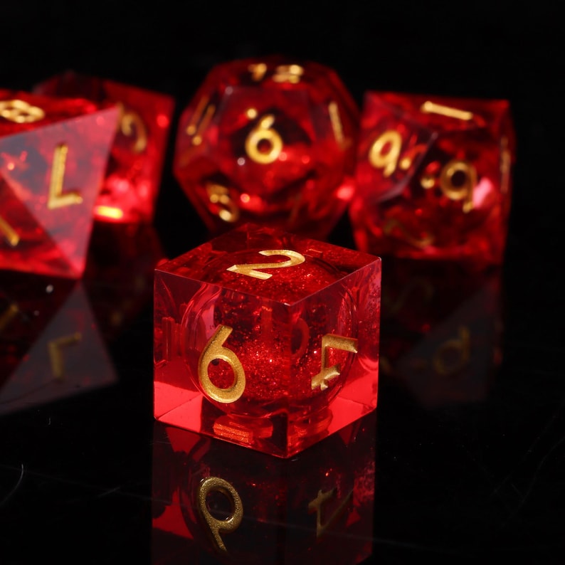 May include: A selection of translucent red dice with gold numerals. The dice are in various shapes, including a six-sided cube and a multi-sided die. The dice are set against a dark background, creating a striking contrast.