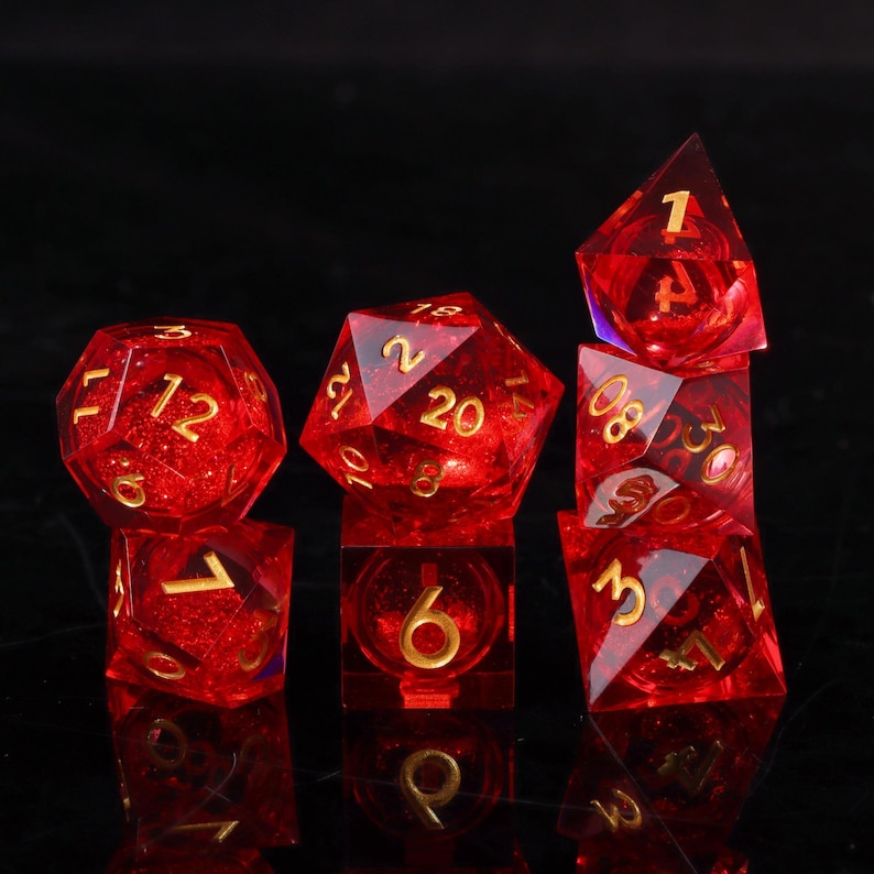 May include: A set of seven red, transparent polyhedral dice with gold numbering. The dice are arranged on a black surface, showcasing their various geometric shapes, including a cube, a d20, and a d4. The dice are designed for tabletop games.