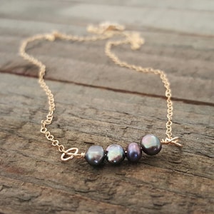 May include: A delicate gold chain necklace with a row of five dark grey pearls.