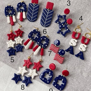 May include: A selection of red, white, and blue earrings with patriotic themes. Designs include star shapes, flag motifs, and geometric patterns. Some earrings feature the letters "USA".