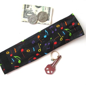 May include: A black fabric key holder with a colorful musical note pattern. The holder has a velcro closure and is shown with a key and a ring.