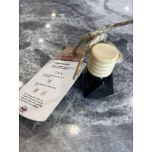 May include: A black, geometric-shaped car air freshener with a light-colored wooden lid and a beige string. A small tag reads "Turkish Mocha" with safety announcements.