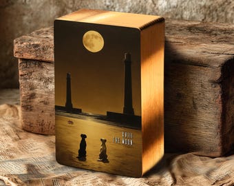 May include: A wooden block with a printed image of a full moon, two lighthouses, and two dog silhouettes. The text "XVIII THE MOON" is printed on the image. The block is sitting on a piece of paper and a wooden box.
