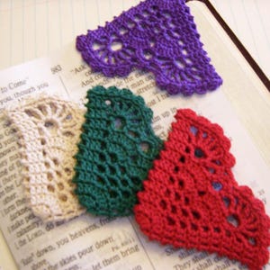 May include: Four crocheted bookmarks in the shape of hearts. The bookmarks are in different colors: purple, green, red, and cream.