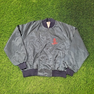 May include: A black nylon bomber jacket featuring a ribbed collar, cuffs, and hem. The front has a snap-button closure and a red embroidered graphic on the chest displaying the Olympic rings and the text "USA" above the rings.