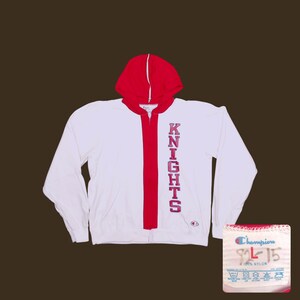 May include: White zip-up hoodie with a red hood and red stripe down the front. The word "KNIGHTS" is printed vertically in red on the front. A Champion tag is visible. The hoodie is made of 100% nylon.