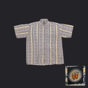 May include: Short-sleeved button-down shirt with a geometric pattern in gray, black, and yellow. The shirt features vertical stripes and a small patch with a drum design. The shirt is made of a lightweight fabric.