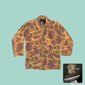 May include: Camouflage pattern jacket in shades of brown, green, and tan. The jacket has a collared neckline and long sleeves. A tag in the lower right corner reads "SMALL 36-38" and "GENUINE STEARNS PRODUCTS".