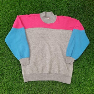 May include: A color-blocked sweatshirt featuring a high neck and long sleeves. The top section is pink, the middle is gray, and the sleeves are blue. The cuffs and neck are gray. This vintage-style sweatshirt is perfect for casual wear.
