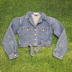 May include: A blue denim jacket with a collared neckline, two chest pockets, and a button-up front. The jacket has long sleeves with buttoned cuffs and a matching belt. The jacket is approximately 20 inches long.