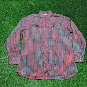 May include: A long-sleeved plaid shirt in red, green, and navy blue. The shirt features a button-down front, two chest pockets, and buttoned cuffs. The fabric has a classic Western style.