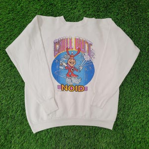 May include: White sweatshirt featuring a cartoon character skiing with the words "CHILL OUT" above and "NOID" below. The graphic is set against a blue and white background with a snowy design. The sweatshirt has long sleeves and a crew neck.