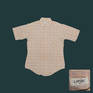 May include: A short-sleeved, button-down shirt with a plaid pattern in beige, white, and light blue. The shirt has a chest pocket and a collar. A small tag with the Levi's logo is visible.
